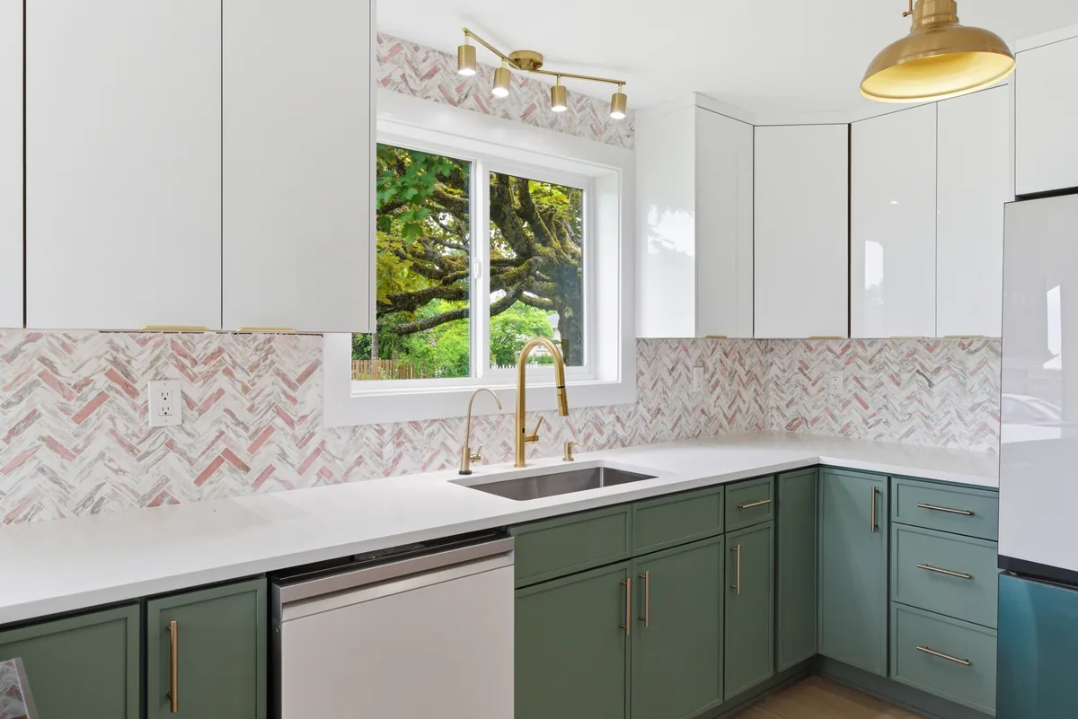 Green kitchen, herringbone backsplash. Marble herringbone run behind the range and around the window, with brass fixtures against green cabinetry.