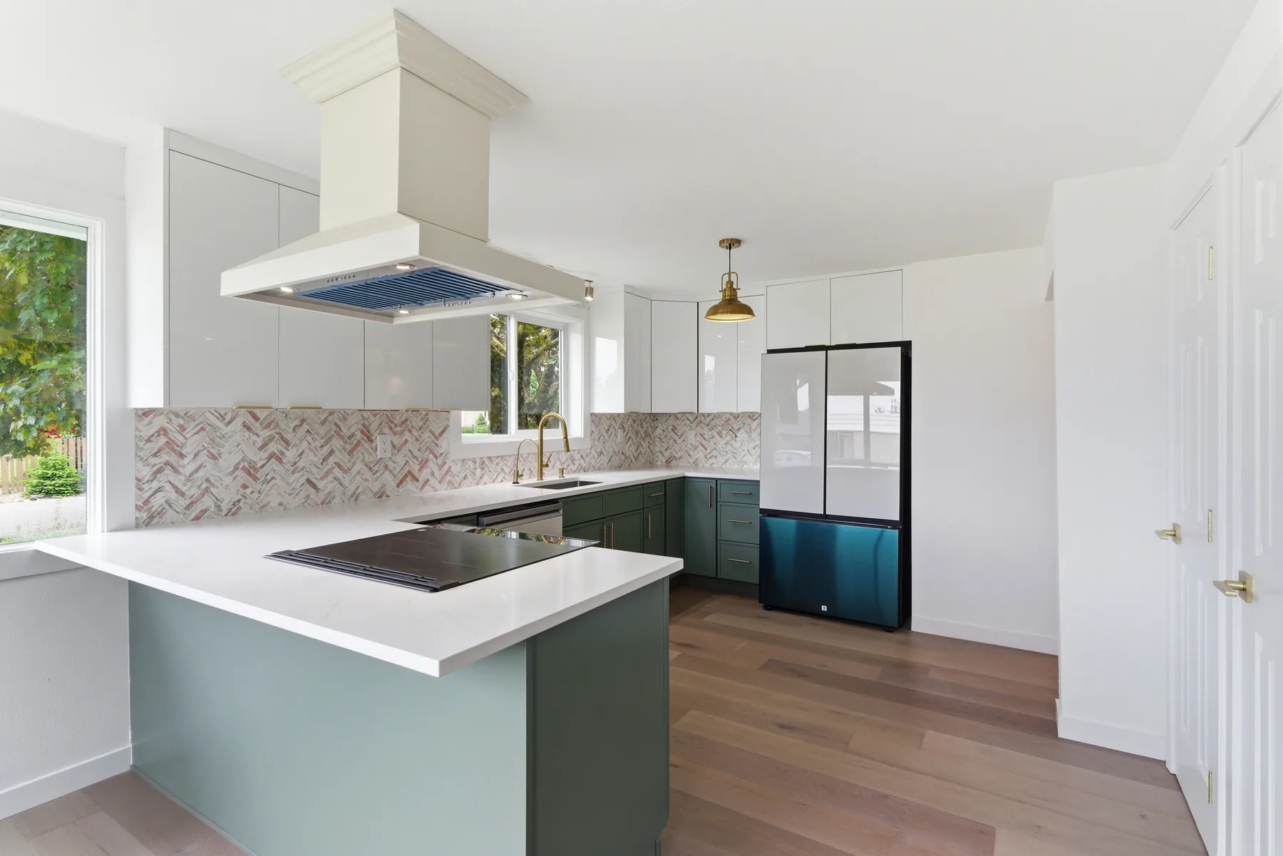 A kitchen finished by Merlan's Tile: green cabinetry, marble herringbone backsplash, brass fixtures and white oak floors.