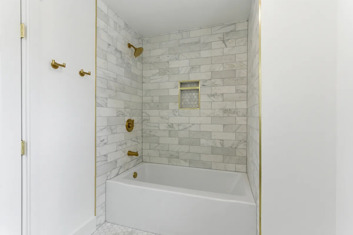 Marble tub surround. Large-format marble with a recessed niche and a brass trim edge.