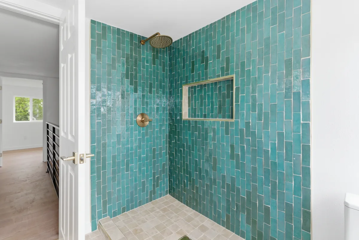 Glazed zellige shower. Full-height glazed tile with a brass rainfall head and a niche cut into the field.